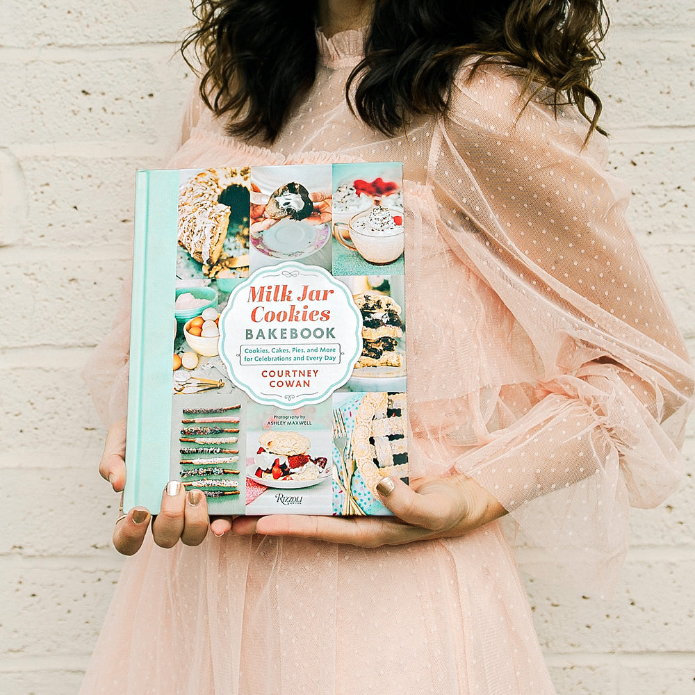 Milk Jar Cookies Bakebook is any baker's new favorite cookbook. Cookbook and bakebook is held by a woman in a dress showing the cover of the cookbook.